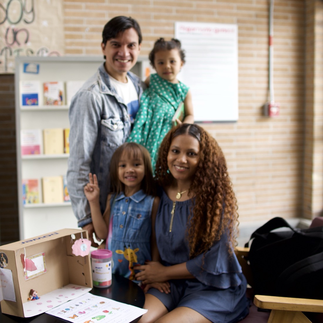 Una familia sonríe en la biblioteca de una sede de Cosmo: el papá carga a la hija menor y la mamá abraza a la mayor.