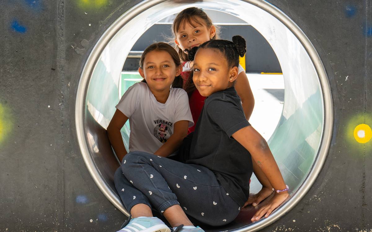 Tres niñas sonríen asomadas a un túnel en el patio de Cosmo.