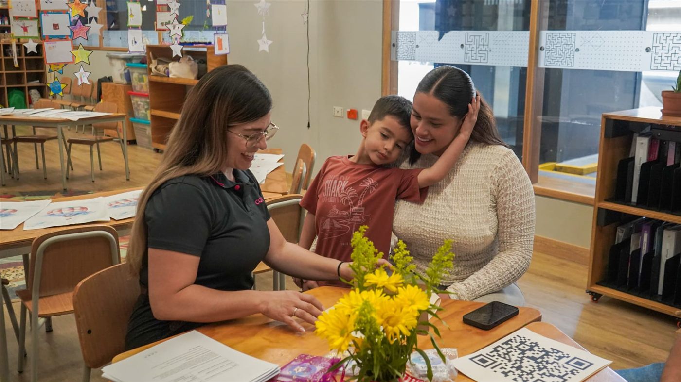 Una docente conversa con una mamá y su hijo en un salón de clase
